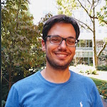 Headshot of a white man with short dark hair and glasses, wearing a blue tshirt.