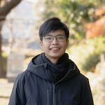 Headshot of an Asian man with glasses standing outside in a black coat and scarf.